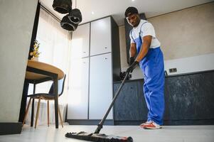 Man janitor with mop in hands from cleaning service washing gray floor in uniform. photo
