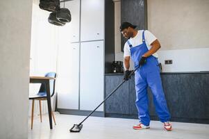 Man janitor with mop in hands from cleaning service washing gray floor in uniform. photo