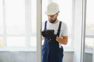 Workman in overalls installing or adjusting plastic windows in the living room at home photo