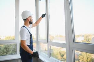 Workman in overalls installing or adjusting plastic windows in the living room at home photo