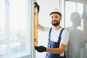 Workman in overalls installing or adjusting plastic windows in the living room at home photo