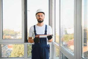 Workman in overalls installing or adjusting plastic windows in the living room at home photo