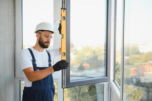 Workman in overalls installing or adjusting plastic windows in the living room at home photo