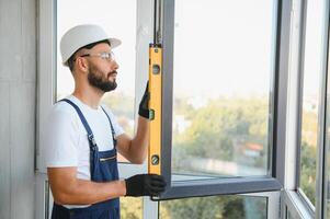 Workman in overalls installing or adjusting plastic windows in the living room at home photo