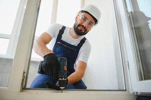 Workman in overalls installing or adjusting plastic windows in the living room at home photo