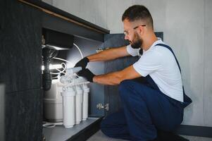 Plumber installs or change water filter. Replacement aqua filter. Repairman installing water filter cartridges in a kitchen. Installation of reverse osmosis water purification system photo