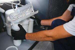 Plumber installs or change water filter. Replacement aqua filter. Repairman installing water filter cartridges in a kitchen. Installation of reverse osmosis water purification system photo