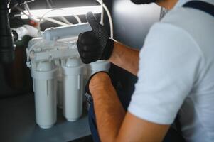 Plumber installs or change water filter. Replacement aqua filter. Repairman installing water filter cartridges in a kitchen. Installation of reverse osmosis water purification system photo