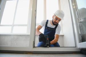 Workman in overalls installing or adjusting plastic windows in the living room at home photo