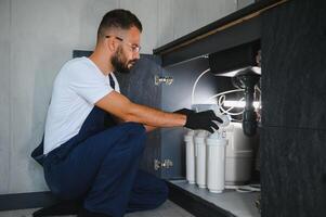 Plumber installs or change water filter. Replacement aqua filter. Repairman installing water filter cartridges in a kitchen. Installation of reverse osmosis water purification system photo