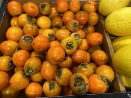 Persimmons in a box on the counter. Persimmons being sold in a store photo