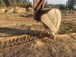 Excavator bucket digs dry sandy soil at a construction site photo