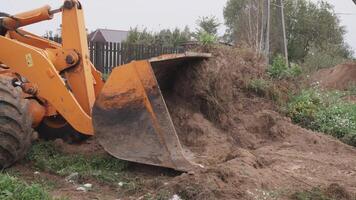 An excavator bucket is actively lifting dirt at a construction site which is surrounded by lush greenery photo