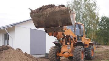 A large construction loader is carefully lifting a bucket that is completely full of soil at a busy building site photo