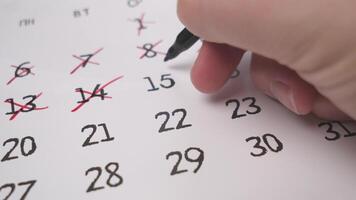 A hand skillfully using a pen to mark significant and important dates on a printed calendar for planning photo