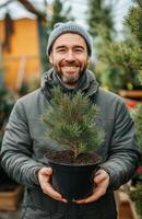 A man holding a small pine tree in a pot photo