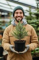A smiling man holding a small tree in a pot photo