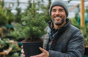 A smiling man holding a small tree in a pot photo