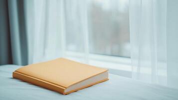 Cozy Reading Session by the Window with Yellow Book in Minimalist Raw Style for Calm and Relaxation Themes in Soft Natural Light Near Sheer Curtains and Blurred Outdoor Views photo
