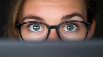 Woman With Glasses Focused on Computer Screen in Dark Room Capturing Modern Technology and Intense Concentration. Emphasizing Eyewear Style, Digital Work Environment, and Eye Expression photo