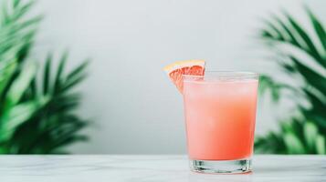 Refreshing Pink Iced Cocktail Drink with Citrus Slice on Marble Table Against Lush Green Palm Leaves photo