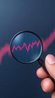 Hand Holding Magnifying Glass Over Digital Stock Market Displaying Red Graph on Dark Background for Trend Analysis and Financial Concept in Vertical Format photo