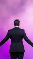 Motivational Speaker in Black Suit Greets Diverse Audience on Stage with Dynamic Purple Lighting Inspiring Energy and Connection Public Speech Conference Event photo