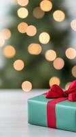 Beautifully Wrapped Christmas Gift Box with Red Ribbon in Front of Blurred Tree with Bokeh Lights Adding Festive Joy and Holiday Warmth for Seasonal Celebrations and Gift-Giving Moments photo