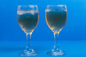 Close-up of two glasses of white wine with ice on a vibrant blue background photo