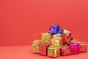 Pile of colorful gifts boxes tied with golden ribbons on a red background photo