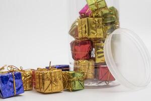 Colorful miniature gift boxes in a clear plastic jar and lying on its side on white background. photo