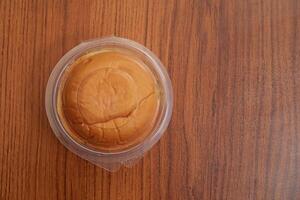 Round butter bun in plastic packaging on a wooden table surface, top view photo