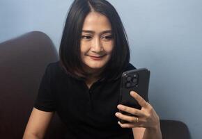 Asian women wearing shirt black sitting on sofa call mobile phone and smiling happy, using online app, shopping on internet photo