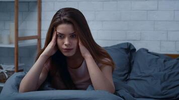 A European woman sits on her bed looking troubled and contemplative. The winter light filters through a window, accentuating her feelings of loneliness and mental distress in her warm home. video