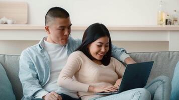 A young man and woman sit closely on a couch, sharing smiles as they engage with a laptop. The cozy indoor setting creates an intimate atmosphere for their activity. video