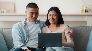 A couple sits closely on a sofa, sharing a joyful moment while using a laptop. They are engaged in a task, surrounded by a cozy home environment with soft lighting. video
