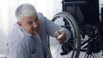 A middle aged man with grey hair is focused on fixing a wheelchair in a well-lit home environment. He appears determined while working on the task at hand, showcasing independence. video