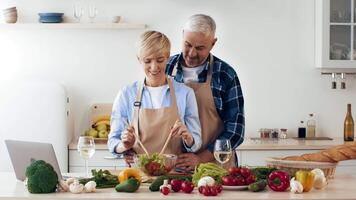 A couple enjoys cooking in their inviting kitchen, mixing fresh vegetables for a salad. The setting features colorful produce, creating a vibrant atmosphere perfect for meal preparation. video