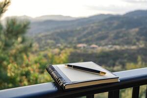 Notebook and Pen on a Fence Overlooking a Green Vast Landscape Capturing Inspiration and Serene Atmosphere photo