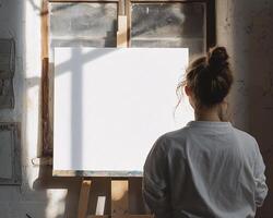 Female Artist in Natural Light Facing a Blank Canvas on an Easel in a Rustic Studio photo