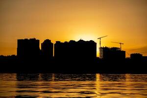 City skyline silhouette during sunset with cranes and buildings reflected in water photo