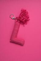 A pink crocheted keychain in the shape of the letter 'L' with a tassel, set against a matching pink background. photo