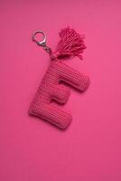 A pink crocheted keychain in the shape of the letter 'E' with a tassel, set against a matching pink background. photo