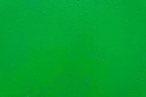 A textured green painted surface with subtle imperfections, rough texture, and small droplets. photo