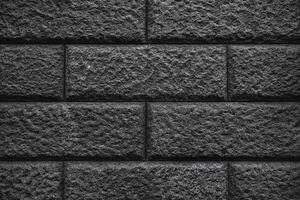 A textured wall of dark gray bricks, with a rough and uneven surface. The bricks are arranged in a traditional pattern. photo