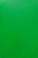A textured green painted surface with subtle imperfections, rough texture, and small droplets. photo