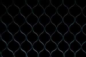 A close-up of a metal fence with a repeating diamond pattern, dark background. photo