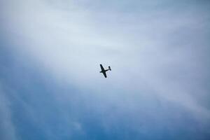 A small airplane flying against a backdrop of a clear blue sky with wispy clouds, creating a serene and open atmosphere photo