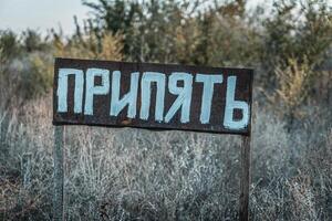 A weathered sign with the word in Cyrillic script, standing in an overgrown, abandoned area. photo