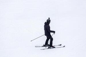 A skier dressed in black gear, including a helmet with a mounted camera, is skiing on a snowy slope, creating a dynamic and adventurous winter sports scene photo